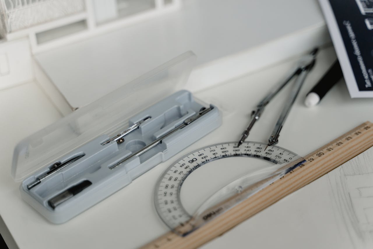 Close-up of architectural drafting tools including compasses, ruler, and paper on a workspace table.